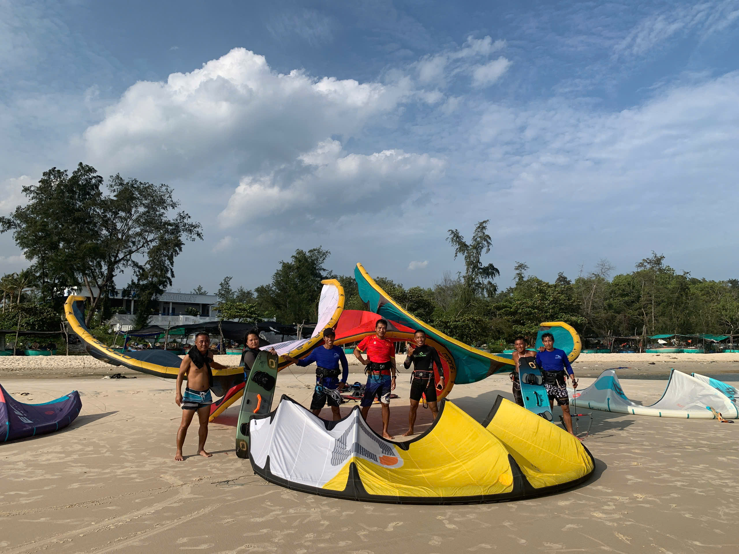 Kiteboarding group standing together beside colorful kites on the beach